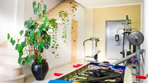 Une salle de sport équipée de matériel d’exercice, avec un escalier et une plante en pot.