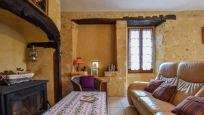 Un salon chaleureux avec une cheminée, un canapé et une table recouverte d’une nappe à motifs floraux.