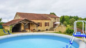 Une maison en pierre avec une piscine, une véranda et un petit jardin.