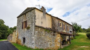 Un bâtiment en pierre avec un toit en pente, une cheminée et un petit porche.