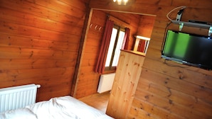 A wooden cabin room with a bed, a television mounted on the wall, and a window with curtains. - Holiday Home in Houyet with Sauna & Garden (Hour)