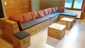 A wooden sofa with cushions, a small wooden bench, and a wooden table in a room with tiled flooring. - Holiday Home in Houyet with Sauna & Garden (Hour)