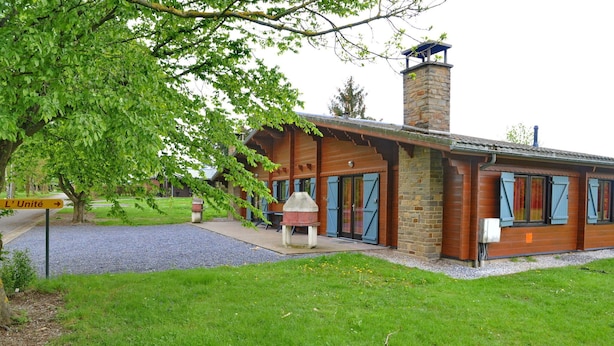 A rustic lodge with a stone chimney, wooden exterior, and a covered outdoor seating area. - Holiday Home in Houyet with Sauna & Garden (Hour)