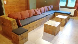 Un canapé en bois avec des coussins, un petit banc en bois et une table en bois dans une pièce dont le sol est recouvert de carreaux.