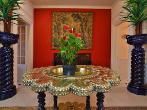 A room with a red wall, a large painting, a table with a decorative base, and two large vases.