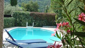 Piscina con sillas de descanso y una sombrilla amarilla, rodeada de follaje y montañas al fondo.