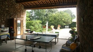 Un patio couvert avec une table de ping-pong, des murs en pierre et des sièges d’extérieur.
