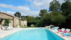 Une piscine avec des chaises longues et un bâtiment en pierre.