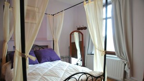 Un lit à baldaquin avec une literie blanche et des oreillers violets, une tête de lit en bois et un miroir au mur.