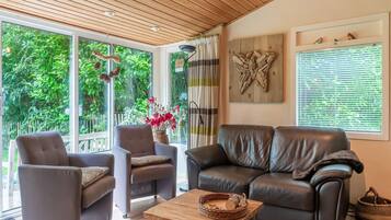 Ein modernes Wohnzimmer mit einer Ledersofa, zwei Sesseln, einem Holztisch und großen Fenstern mit Blick ins Grüne.