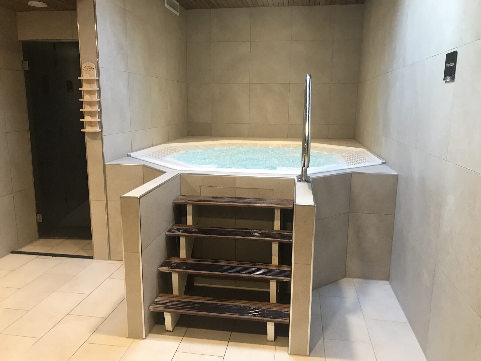 A modern bathroom with a freestanding bathtub, wooden steps, and a tiled floor.