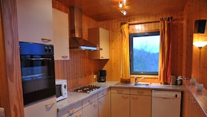 Een kleine keuken met houten wanden, een ingebouwde oven, een magnetron, een kookplaat, een spoelbak en een raam met gordijnen.