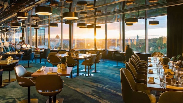 Een modern restaurant met grote ramen, meerdere eettafels en hangende lampen.