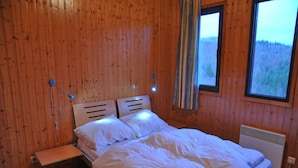 Een slaapkamer met houten lambrisering, een bed, een raam en een verwarming.