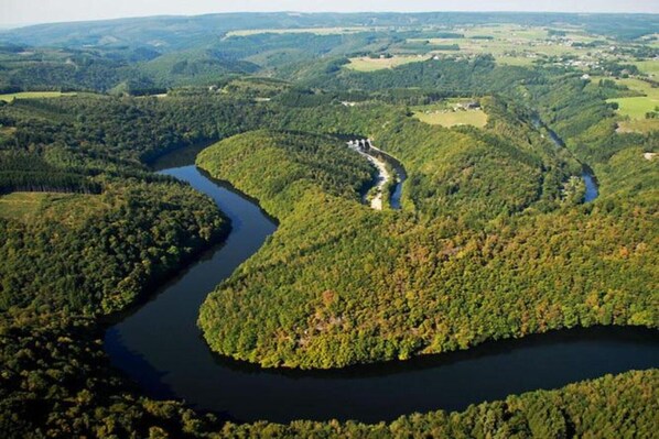 An aerial view of a river winding through a densely forested area with a small settlement visible along the riverbank. - Holiday Home in Houffalize with Valley Views (Houffalize)
