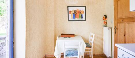 Uma pequena área de refeições com uma mesa e cadeiras, um quadro na parede e uma porta de madeira.