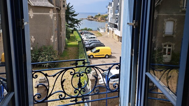 Blick vom Balkon auf eine Küstenstraße mit parkenden Autos und Gebäuden.