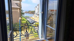 Blick aus einem Fenster auf eine Küstenstraße mit parkenden Autos und Gebäuden.