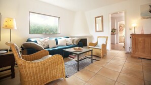 Un salon comprenant un canapé, deux fauteuils en osier, une table basse et une grande fenêtre.