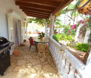 Un patio techado con piso de piedra, una parrilla, sillas de mimbre y una mesa con una planta en maceta.