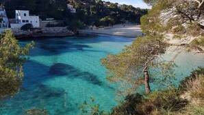 Un paysage côtier avec une eau turquoise cristalline, une plage de sable et des bâtiments situés sur une colline.