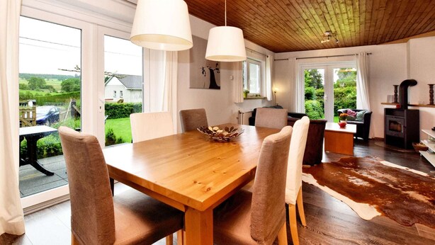 A dining area with a wooden table and chairs, large windows, and a view of the outdoors. - Wellness Escape in Gouvy (Gouvy)