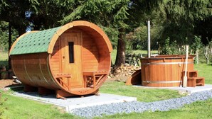 A wooden barrel-shaped building with a green roof, a small door, and a bench outside. - Wellness Escape in Gouvy (Gouvy)
