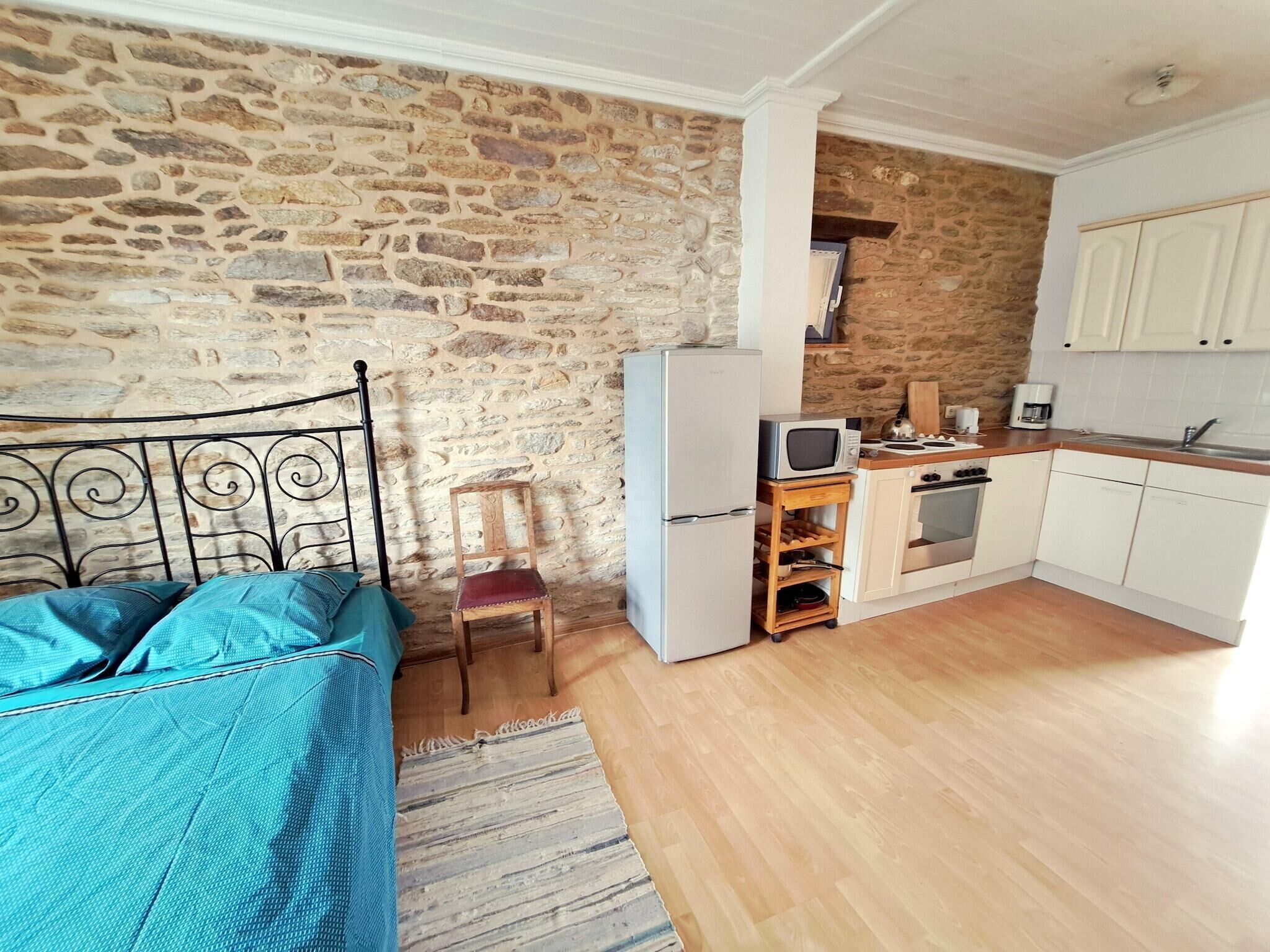 Une cuisine compacte avec un mur en pierre, un lit avec une literie bleue et une petite chaise en bois.