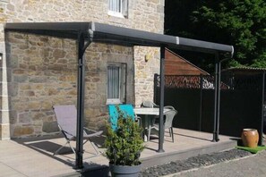 Relax in this serene outdoor seating area with a table and chairs, surrounded by lush greenery and a shaded structure.
