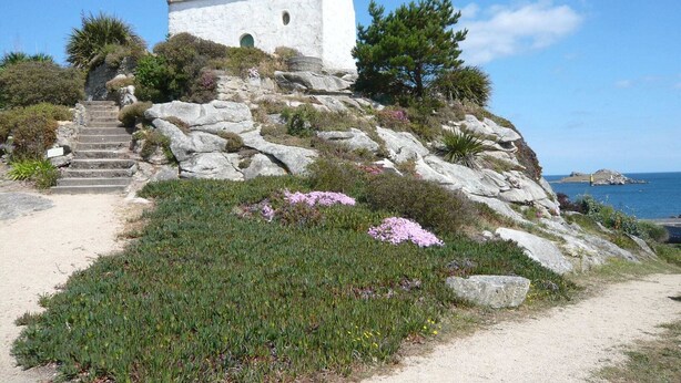 Une église blanche dotée d’un clocher, située sur une colline rocheuse et offrant une vue dégagée sur la mer.