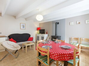 A cozy dining area with a red polka dot tablecloth, wooden chairs, a sofa, and a television.