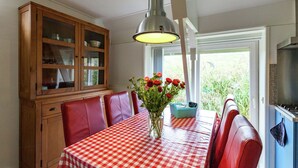 Un comedor con mantel a cuadros rojos y blancos, sillas de cuero rojo, un mueble de madera con puertas de cristal y una lámpara colgante.