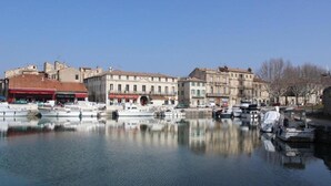 A marina with boats docked, buildings with commercial establishments, and a clear sky. - Mediterranean Garden Retreat (Vergèze)