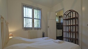 A bedroom with two beds, a radiator, a window with curtains, a wooden screen, and a bathroom visible through an open door. - Mediterranean Garden Retreat (Vergèze)