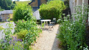 Een grindpad leidt naar een witte tafel en stoelen in een tuin vol planten en bloemen.