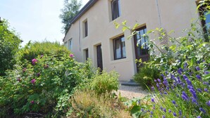 Een gebouw met twee verdiepingen, met een beige gevel, omgeven door weelderige begroeiing en bloeiende planten.