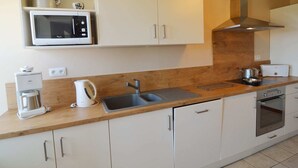 Een kleine keuken met witte kastjes, een magnetron, een waterkoker, een broodrooster en een fornuis.