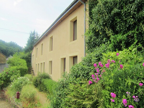 A building with a beige facade, multiple windows, and a garden with pink flowers. - Modern Farmhouse in Chassepierre with Terrace (Chassepierre)