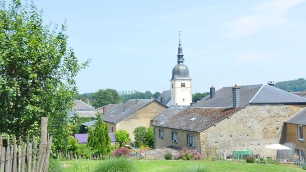 Een landelijk dorp met stenen huizen, een kerk met een klokkentoren en een omheind tuingebied.