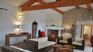 A cozy living room with wicker furniture, a fireplace, and a stone wall. - Cosy holiday home with views and private pool (Saint-Ambroix)