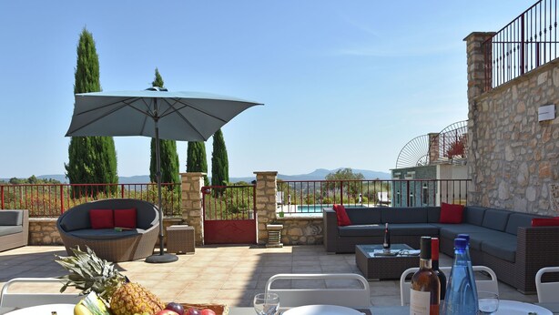 An outdoor patio with a dining setup, including a table with plates, cutlery, and a bottle of water, surrounded by wicker furniture and a stone wall. - Cosy holiday home with views and private pool (Saint-Ambroix)