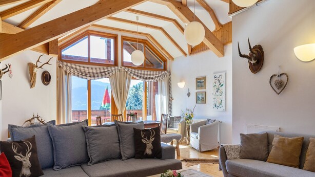 Een gezellige woonkamer met hoog houten plafond, een zithoek, een bijzettafeltje en uitzicht op het groen door grote ramen.