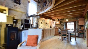Una cocina rústica con vigas de madera, una pared de piedra y un comedor con mesa y sillas de madera.