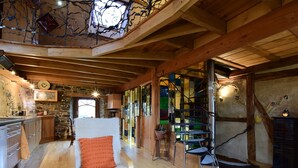 Un interior rústico con techo de madera, una silla blanca con cojín naranja, una mesita de centro de madera y una pequeña planta.