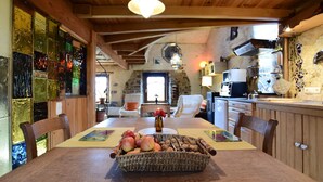 Un comedor rústico con una mesa de madera, una cesta de manzanas y una pared de piedra al fondo.