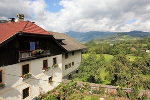 Un chalet traditionnel avec un toit rouge, de nombreuses fenêtres et des jardinières sur le balcon.