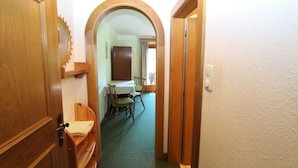 Un pasillo estrecho con puertas de madera y un arco que da a un comedor con una mesa y sillas.
