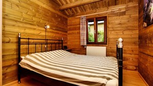 Un dormitorio de cabaña de madera con una cama, una ventana con cortinas y un radiador.