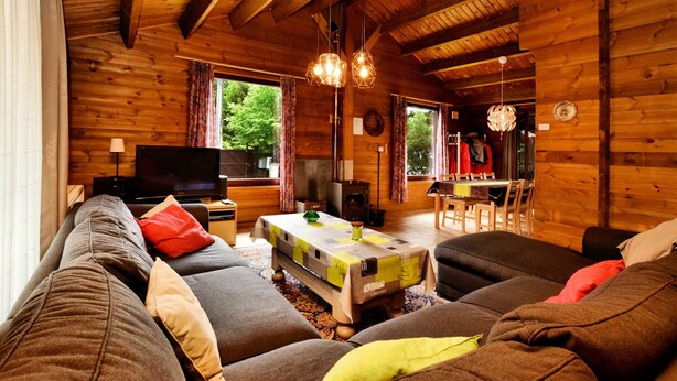 Un interior de cabaña acogedor, con detalles de madera, un sofá, un televisor y una zona de comedor.