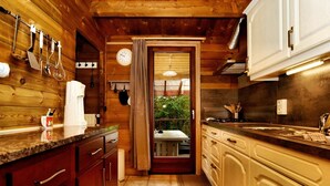 Un interior de madera con una zona de cocina, que incluye armarios, una encimera y un ventanal con vistas al follaje exterior.